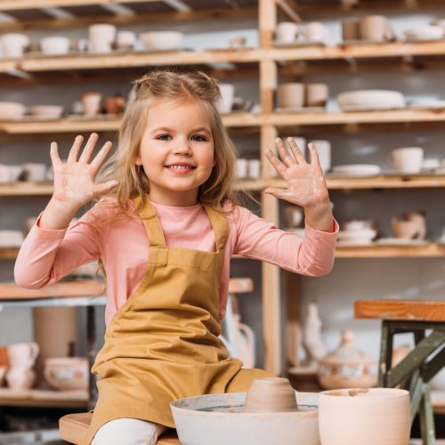 adorable smiling child with clay of pottery wheel showing hands in workshop