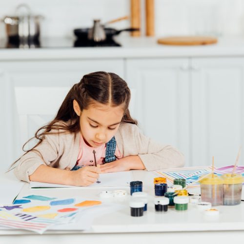 concentrated and cute kid painting on paper at home