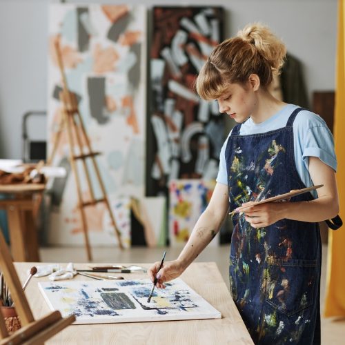 Young inspired woman in apron painting with acrylic paints